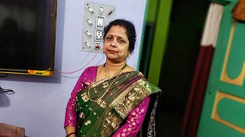Rinku Tarafdar at her house in a pink and green saari. She is standing in front of a blue wall and green door.