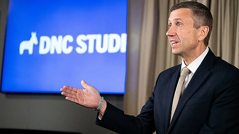 Chair Ken Martin in a suit gestures while speaking in front of a blue screen displaying "DNC STUDIO" with a donkey logo. The setting is professional and formal.