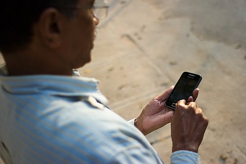 Indian man in blue shirt and spectacles using a touch phone. over the shoulder.