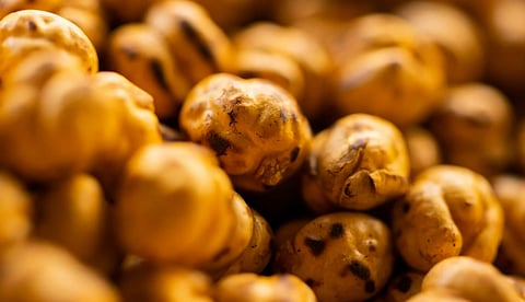Close-up of roasted chickpeas with a golden-brown hue and charred spots. The image conveys a warm and crunchy texture, highlighting a savory snack.