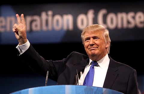 Image of President Donald trump showing peace sign at the 2013 Conservative Political Action Conference (CPAC) in National Harbor, Maryland. he is wearing a black suit with blue tie.