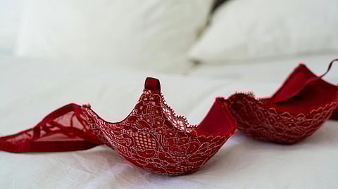 Red lace bra on unmade white bed with two pillows in the background, conveying a sense of intimacy and relaxation in a cozy bedroom setting.