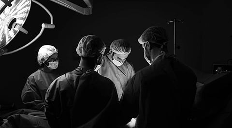 Black and white image of four surgeons in an operating room, focused under a bright surgical light. Their expressions convey concentration and teamwork.