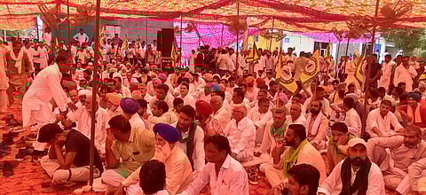 A group of farmers wearing mostly white clothes sit under a red tent at a protest.