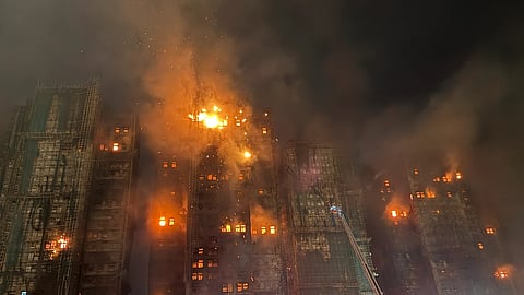 Nighttime high-rise fire with intense flames and thick smoke engulfing upper floors. Aerial ladder reaches up, highlighting a dramatic emergency scene.