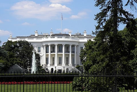The White House with its iconic columns, surrounded by lush greenery and a fountain, under a blue sky with fluffy clouds. A peaceful, historic scene.