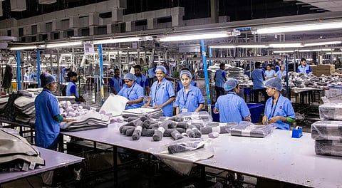 Workers in blue uniforms and hairnets organize and package textiles on large tables in a well-lit garment factory, conveying teamwork and productivity.