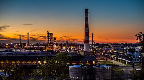 Image of Moscow oil refinery. image depicts Industrial skyline at sunset with smokestacks and refinery, silhouetted against an orange and blue sky. The scene conveys a busy yet serene atmosphere.