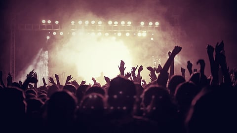 A vibrant concert scene with an enthusiastic crowd raising hands against bright stage lights and smoke, creating an energetic and lively atmosphere.