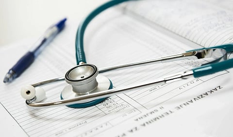 A teal stethoscope rests on open medical charts, alongside a blue pen. The scene conveys a professional, clinical atmosphere, emphasizing healthcare themes.