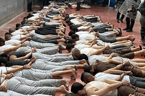 Palestinian prisoners lying facedown in a prison with their hands tied behind their backs while soldiers in riot gear walk nearby.