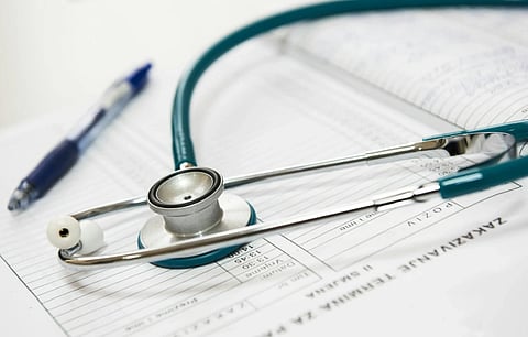 A stethoscope rests on open medical forms with a blue pen nearby. The setting conveys a professional and clinical atmosphere, indicating healthcare documentation.