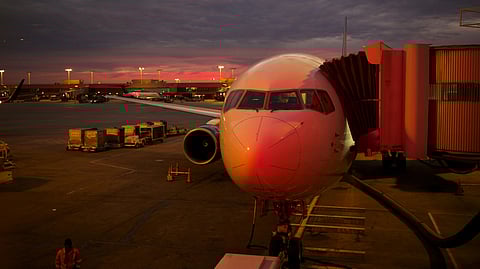 Airplane at airport gate during sunset, with vivid orange and pink hues in the cloudy sky. The mood is calm and anticipatory, highlighting travel.