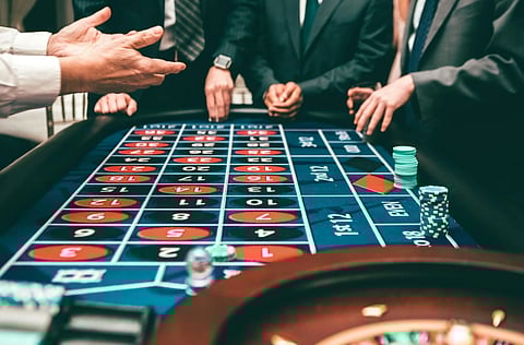 People in formal attire stand at a roulette table, placing bets. Chips are stacked nearby, creating an atmosphere of tension and anticipation.