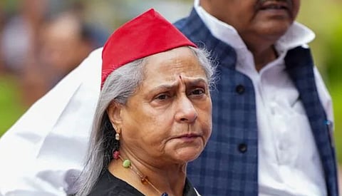 Image of veteran actress Jaya Bachchan in a red cap appears thoughtful and serious; she is outdoors, accompanied by a man in a blue plaid vest.