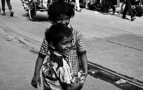 Two young boys, joyfully smiling, stand close together on a bustling street. The image is black and white, capturing a lively, playful moment.