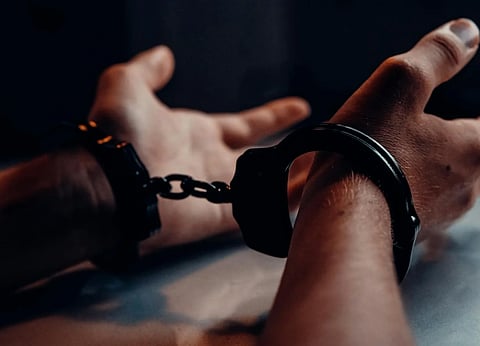 Hands in handcuffs rest on a table in dim light, conveying a serious and somber mood, with shadows emphasizing tension and confinement.