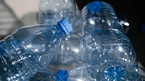 A pile of crumpled plastic bottles with blue caps, glistening with droplets of water. 