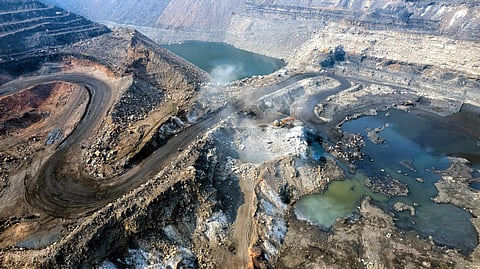 Aerial view of an open-pit mine with winding dirt roads, exposed rock layers, and scattered pools of water.