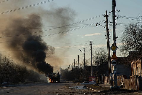A burning vehicle emits thick black smoke on an empty street lined with utility poles and bare trees. The scene conveys a sense of desolation and urgency.