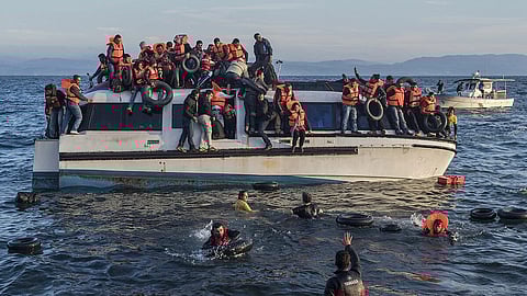 A crowded boat in the sea is filled with people in orange life jackets, some in the water holding onto life rings. The scene is urgent and tense.