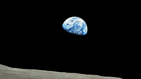 View of Earth rising over the Moon's barren, gray surface against a vast, black space. Earth appears as a small blue and white sphere, evoking awe and wonder.