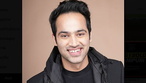 In the image Raj Shamani is shown smiling in the camera wearing a black top and jacket the background is of pinkish colour