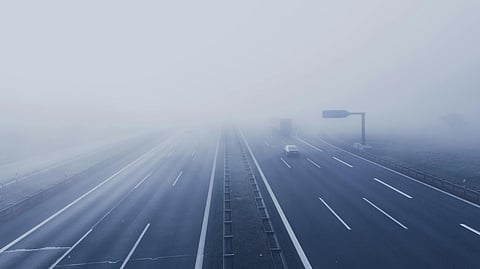 Foggy highway scene with minimal traffic, including a car and a truck, under an overcast sky.