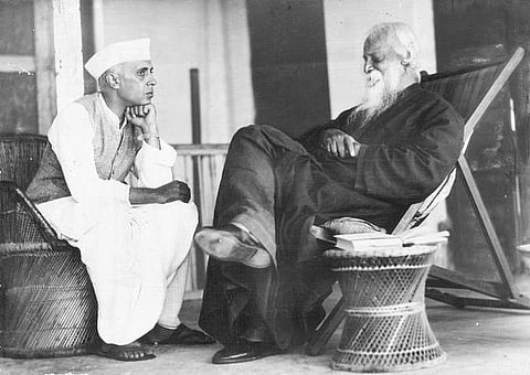 Jawaharlal Nehru is sitting with Rabindranath Tagore. He is sitting in the left, with is hand placed on this chin, while Tagore has folded hands and is smiling.