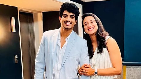 Palash Muchhal and Smriti Mandhana pose for a picture together smiling as Smriti holds Palash's hand. Palash is wearing a light blue suit, and Smriti a white striped outfit.
