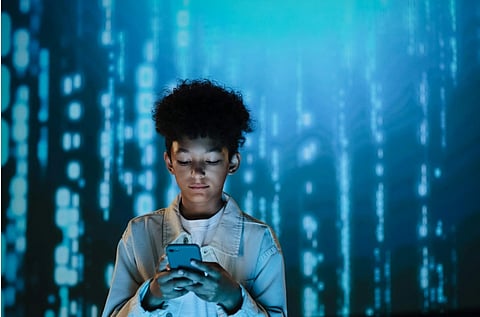 A young person stands focused on a smartphone, surrounded by a digital background with cascading blue code.
