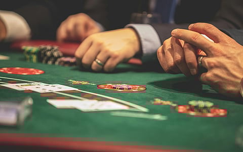 Close-up of a poker game in progress, showing three players' hands, chips, and cards on a green table. The atmosphere is tense and focused.