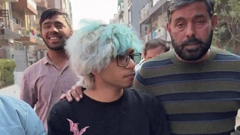 In the image many people are shown taking a teenager somewhere the teenager's hair are white and blue