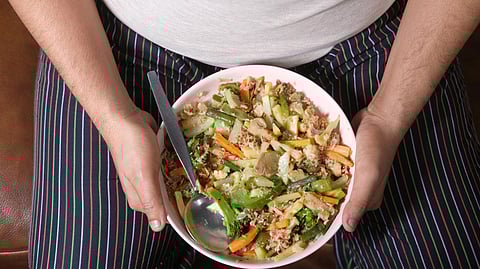Person in striped pants holding a bowl of mixed vegetables, including carrots, green beans, and broccoli, with a spoon.