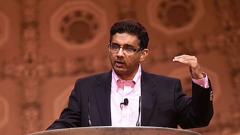 Dinesh D'souza speaking at a podium during the Conservative Political Action Conference. He gestures with one hand, appearing engaged and focused.