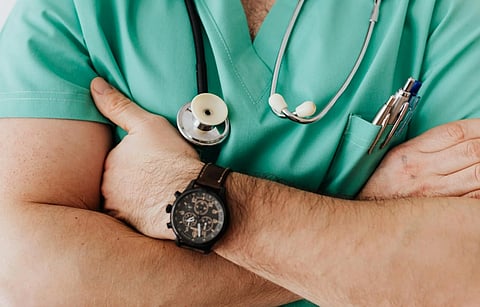 Close-up of a healthcare professional in green scrubs with arms crossed, wearing a stethoscope and pens in the pocket; exudes confidence and professionalism.