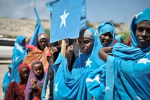 Somalian women are holding their country's flag, in blue and white dress. There are a couple of young children also.