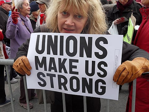 A woman showing a "unions make us stronger" sign at a protest.