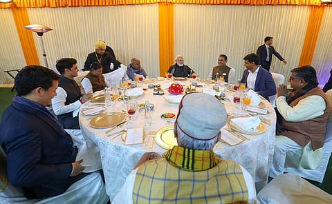 PM Modi is seated with other NDA MPs at a roundtable dinner feast. The dinner table is set very beautifully, with shiny utensils and menu alongside. 