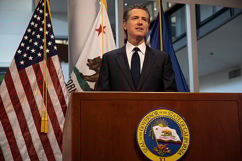 Gavin Newsom speaking at a podium. Flag of the US is behind him.