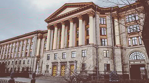 A grand neoclassical building stands with tall columns and an ornate facade. The overcast sky and bare trees add a somber, historic tone.