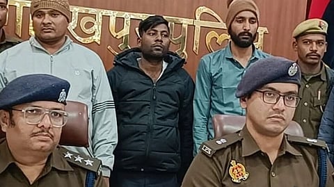 Two policemen in uniform are seated at a desk during the press-conference after the arrest of the three men in casual clothes standing at the back. There is also a police logo in the backdrop.