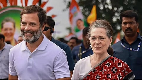 In the image Rahul Gandhi and Sonia Gandhi are shown smiling and walking Rahul Gandhi is wearing a white t-shirt and Sonia Gandhi is wearing Saree