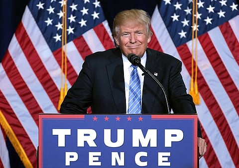 Image of US president Donald Trump speaking at an immigration policy speech in Phoenix, Arizona. in the image he standing in front of a podium which says 'Trump Fence'. There are US national flags behind him. 