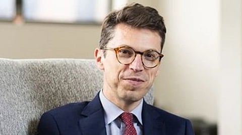 Image of MIT professor Nuno F. Gomes Loureiro. In the image 
he is wearing a suit and glasses sits on a gray chair in an office, smiling softly. 
