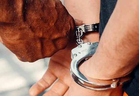 A close-up of a person in handcuffs, their hands positioned behind their back. Another hand is securing the cuffs, conveying a serious tone.