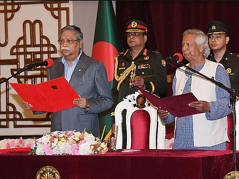 The image shows Bangladesh President Mohammad Shahabuddin administering the oath of office to Dr. Muhammad Yunus, the Chief Advisor of the interim government, at the Darbar Hall of Bangabhaban in Dhaka, in 2024. Two Army Officers are standing behind them.