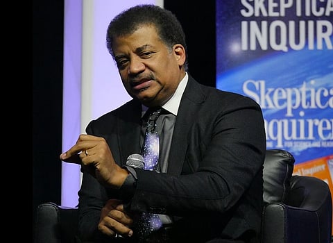 Image of Neil deGrasse Tyson at CSICon 2022. he wearing a black suit and a space themed tie. he is holding a mic and bheind him a text is written skeptical inquiries.