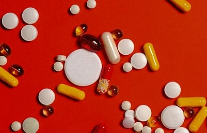 Various pills and capsules in white, yellow, and brown scattered on a vibrant red background, conveying a sense of health and medicine.