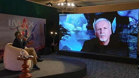 Tollywood Director S.S. Rajamouli on stage having a discussion through video call on a large screen with Hollywood Filmmaker James Cameron. IMAX backdrop visible.